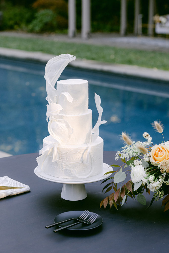 What to Ask Your Wedding Planner - an informative post with an image of an all-white cake backdropped by a deep blue pool